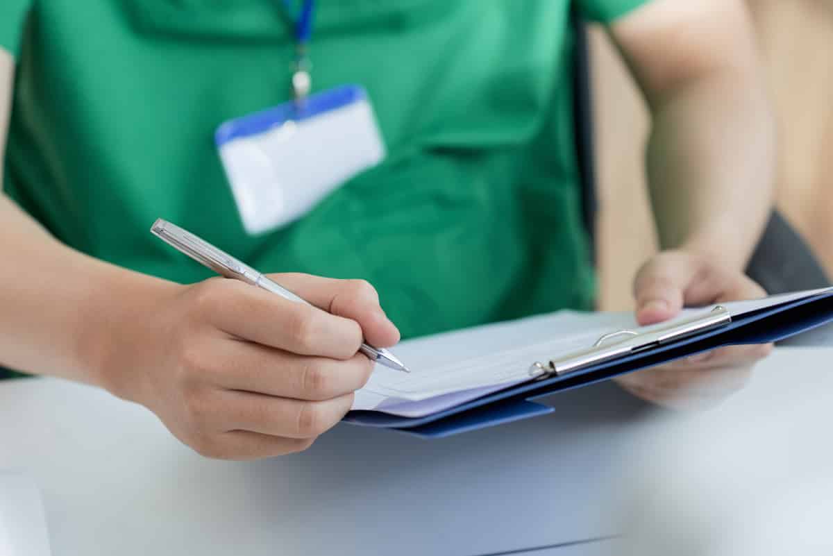 A doctor holding on and writing down notes onto his chart